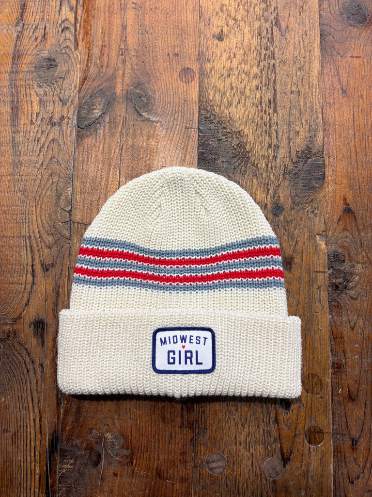 White knit beanie with red and blue stripes and 'Midwest Girl' label on a wooden surface