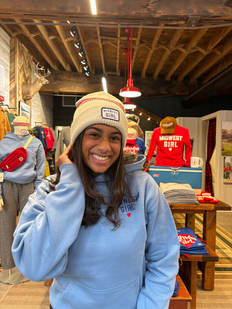 Person wearing a blue sweatshirt with a logo, standing in a store with various items and products in the background.